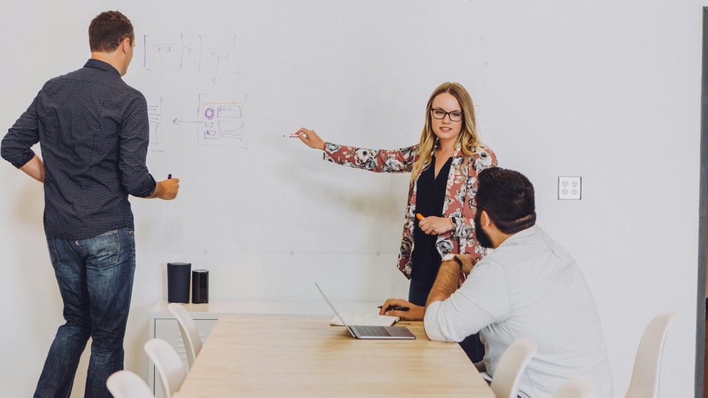 femme qui pointe un tableau et échange avec deux personnes