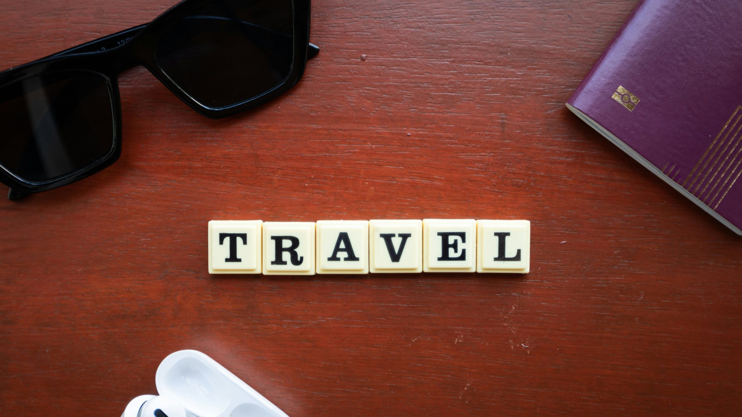 lettre scrabble travel sur un bureau avec une paire de lunette noir et un passeport